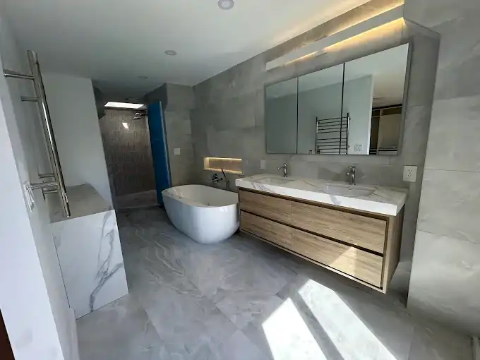 Bathroom with a wood-finish double vanity, freestanding bathtub and illuminated mirrors.