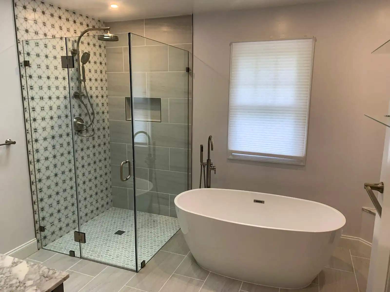 Bathroom with a freestanding bathtub, glass shower enclosure and patterned tile wall.