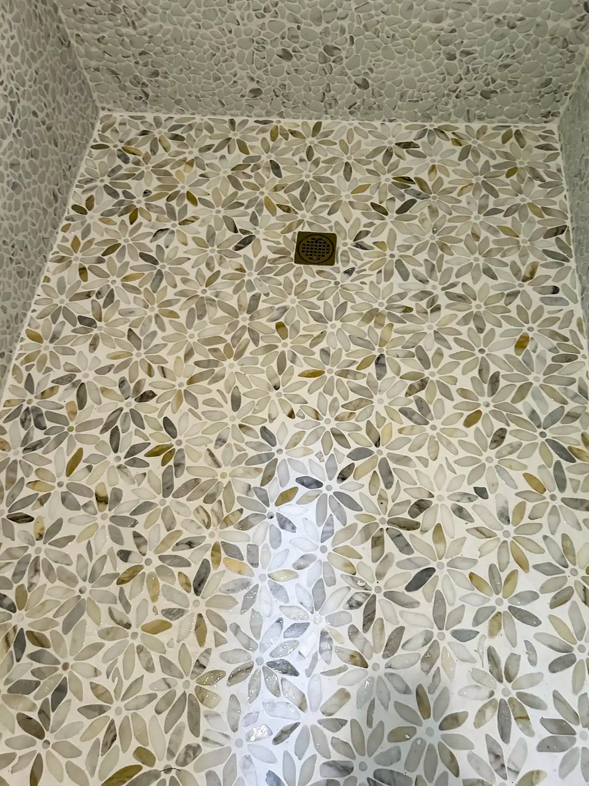 Decorative mosaic shower floor with a central drain and pebble-style tile edging.