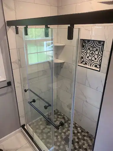 Glass shower enclosure with a black frame, wall niche and patterned shower floor.