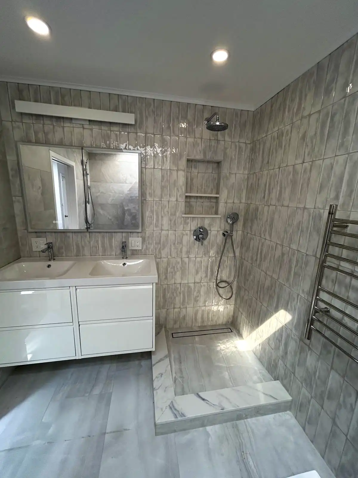 Gray-tiled bathroom with a white vanity, shower fixtures and towel radiator.