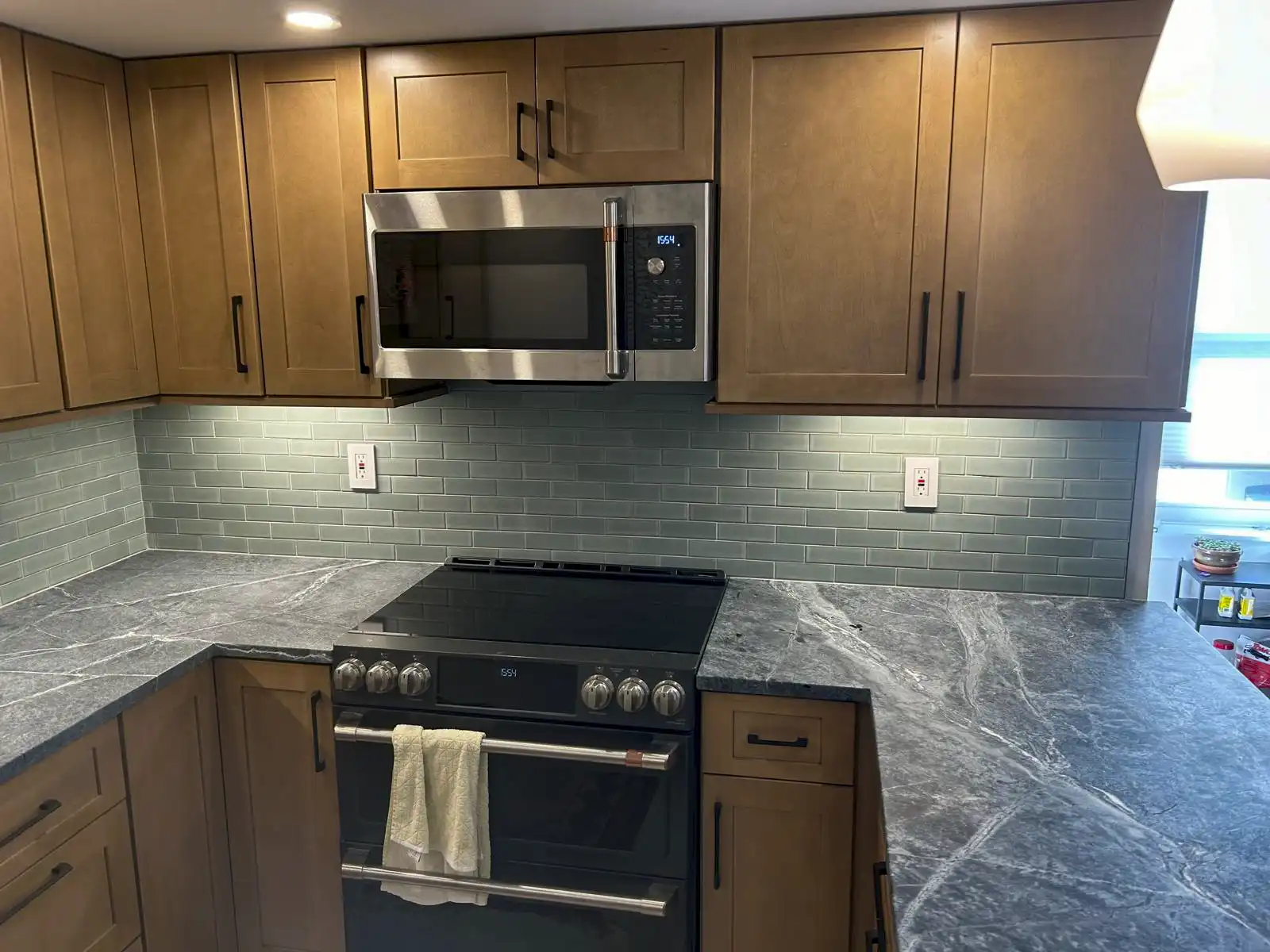Wood-finish kitchen cabinets above a tiled backsplash, range and stone-look countertop.