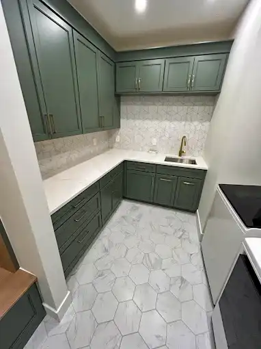 Green laundry room cabinets and a sink above hexagonal floor tiles.