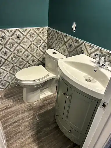 Powder room with a gray vanity, patterned wall tiles and dark green walls.