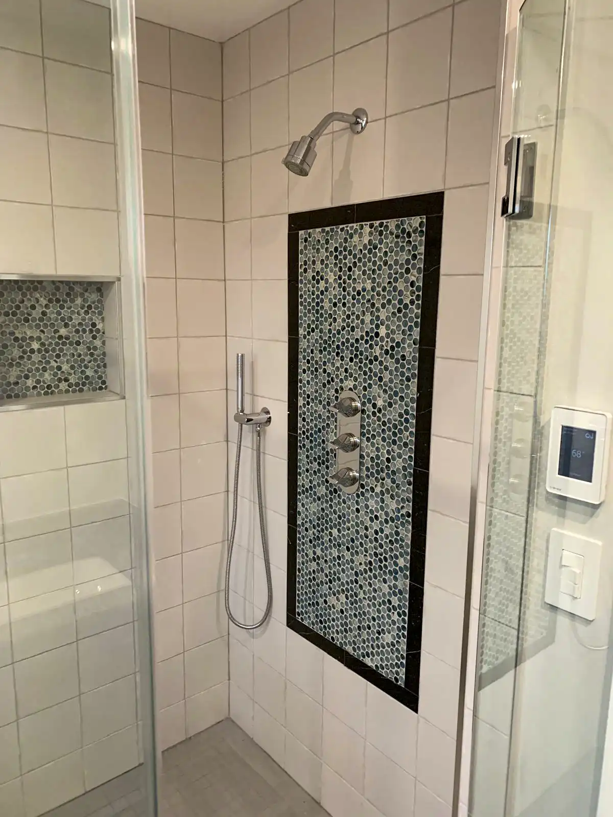 Shower wall tiles with a dark mosaic accent panel, niche and glass screen.
